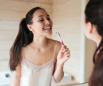 Woman brushing teeth after teeth whitening in Baltimore