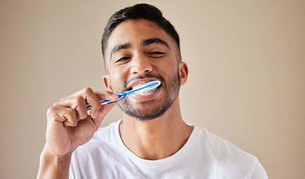 Man smiling while brushing his teeth