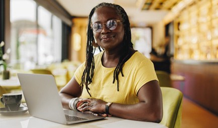 Woman in yellow shirt smiling while working on laptop
