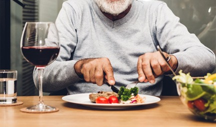Smiling man using fork and knife to cut dinner