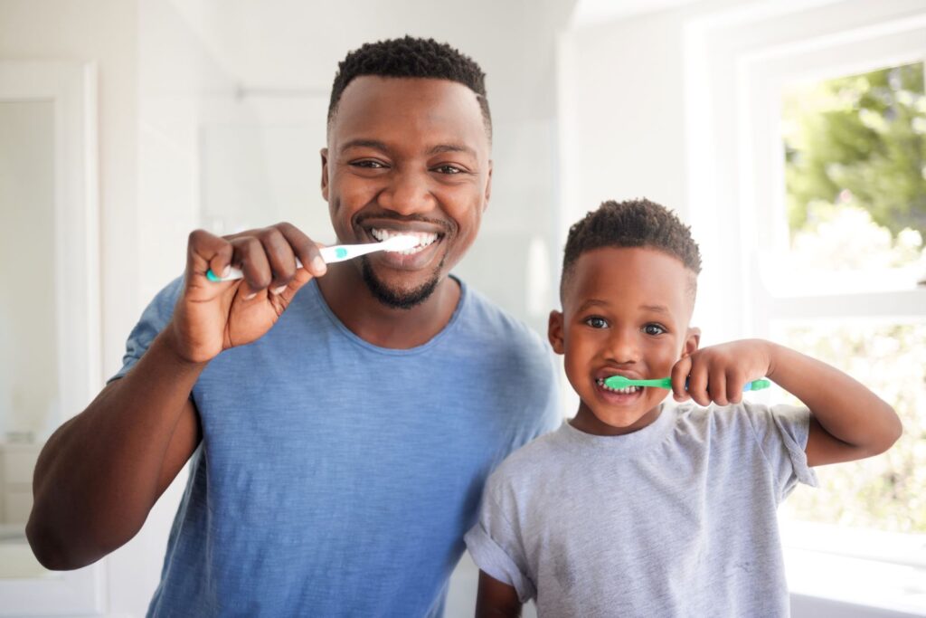 A father and son brushing their teeth together.